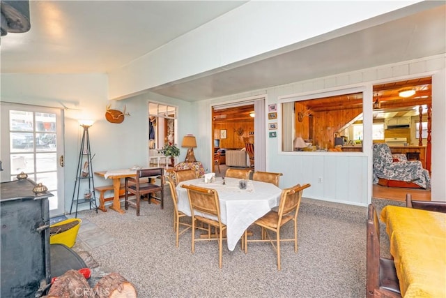 carpeted dining room featuring vaulted ceiling and wooden walls