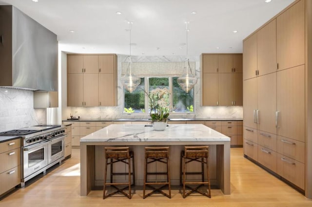 kitchen featuring a center island, range with two ovens, wall chimney range hood, light wood-type flooring, and a breakfast bar