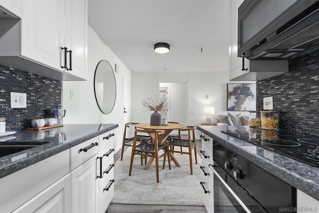 kitchen with decorative backsplash, cooktop, white cabinetry, hardwood / wood-style flooring, and dark stone counters