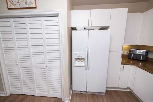 kitchen featuring dark wood-type flooring, white cabinetry, white refrigerator with ice dispenser, and dark stone counters