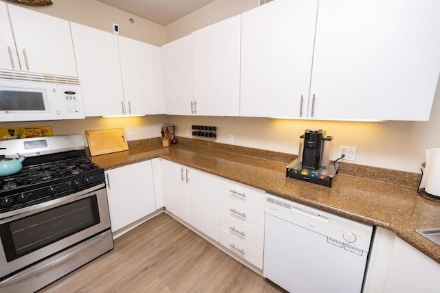 kitchen with dark stone countertops, light hardwood / wood-style floors, white cabinets, and white appliances