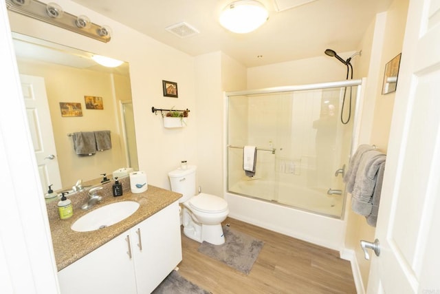 full bathroom featuring hardwood / wood-style flooring, bath / shower combo with glass door, vanity, and toilet