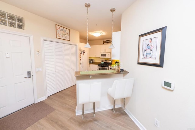 kitchen featuring a breakfast bar area, white cabinets, hanging light fixtures, kitchen peninsula, and stainless steel gas range