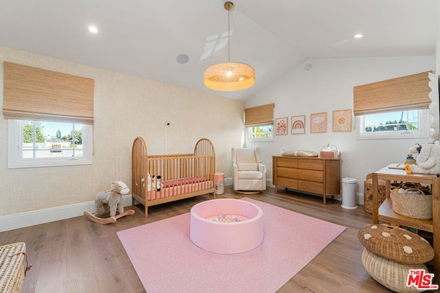 bedroom with a nursery area, vaulted ceiling, and hardwood / wood-style floors