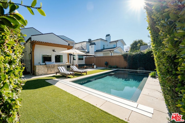 back of property with an outdoor bar, an outdoor kitchen, a lawn, and a patio