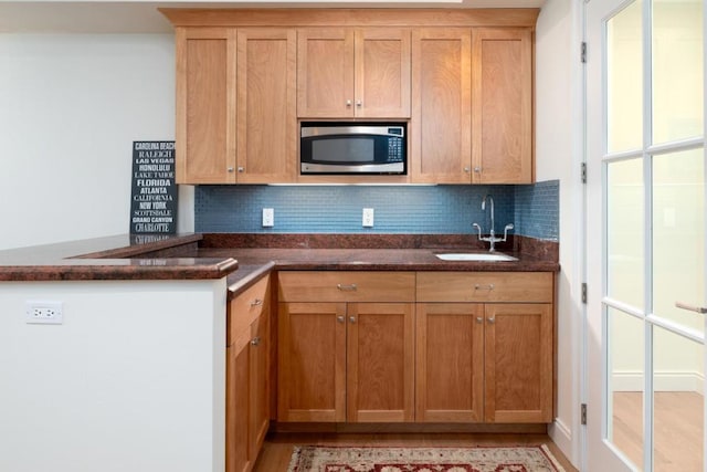 kitchen with stainless steel microwave, kitchen peninsula, sink, and decorative backsplash