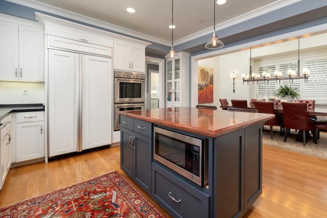 kitchen featuring crown molding, built in appliances, hanging light fixtures, light hardwood / wood-style floors, and white cabinets