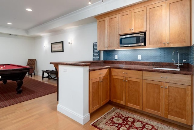 kitchen with sink, a tray ceiling, light hardwood / wood-style floors, decorative backsplash, and kitchen peninsula