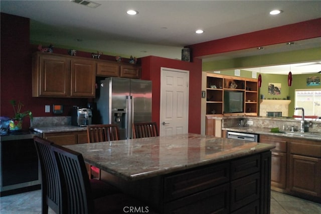 kitchen featuring stainless steel appliances, a kitchen island, sink, light stone counters, and a kitchen bar