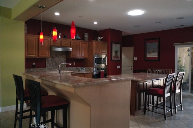 kitchen featuring a kitchen bar, sink, backsplash, decorative light fixtures, and kitchen peninsula