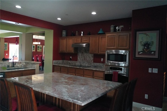 kitchen with appliances with stainless steel finishes, sink, light stone countertops, and a center island