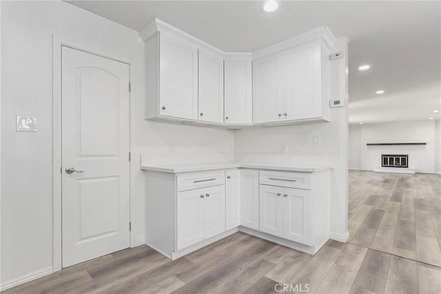 kitchen featuring light wood-type flooring, a brick fireplace, and white cabinetry