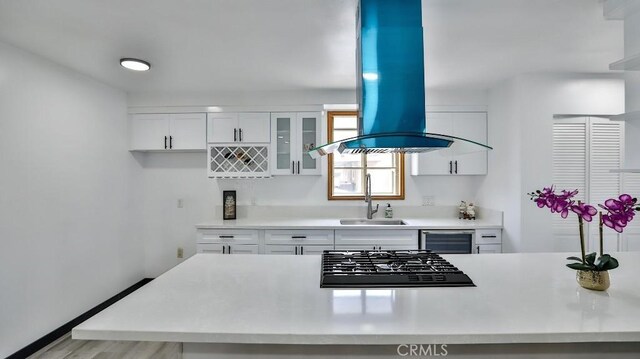 kitchen featuring black gas cooktop, light countertops, island exhaust hood, white cabinetry, and a sink