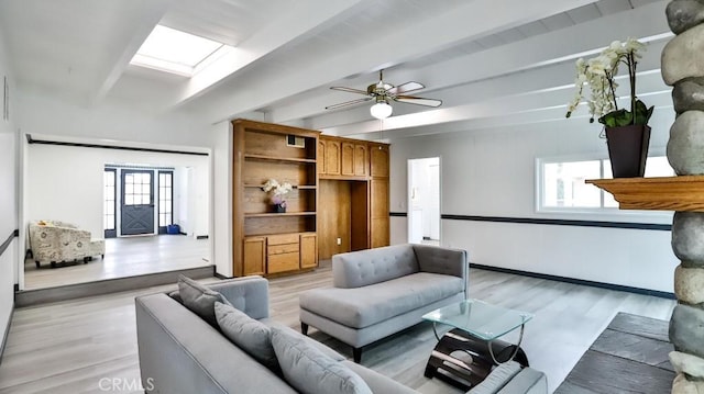 living area with beam ceiling, a skylight, light wood finished floors, and ceiling fan