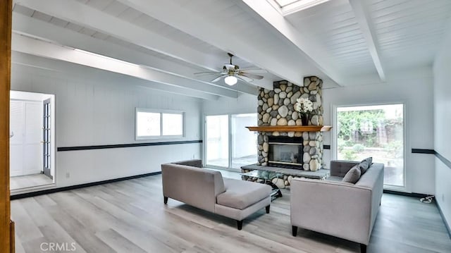 living area with beam ceiling, a stone fireplace, light wood finished floors, baseboards, and ceiling fan