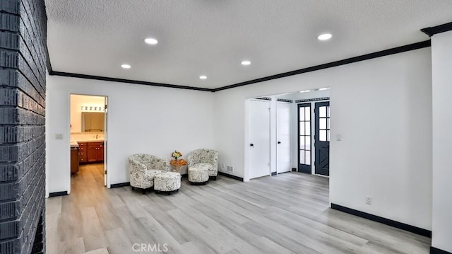 sitting room featuring light wood-type flooring, baseboards, a textured ceiling, and crown molding