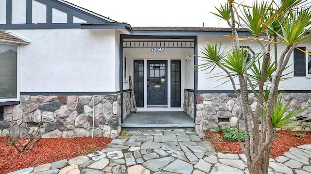 view of exterior entry featuring stone siding and stucco siding