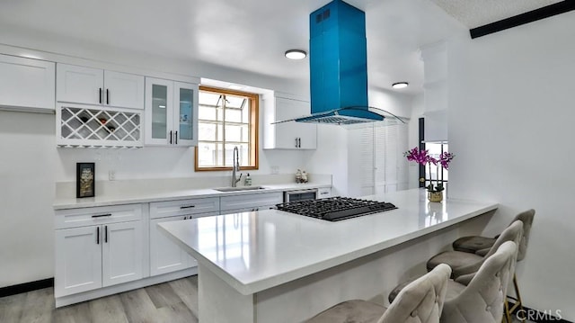 kitchen featuring black gas stovetop, a kitchen breakfast bar, white cabinetry, a peninsula, and island range hood