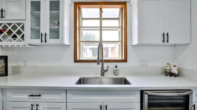 kitchen featuring wine cooler, light countertops, glass insert cabinets, and a sink