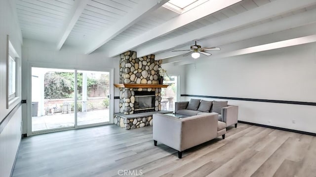 living room featuring beamed ceiling, a skylight, a fireplace, and light wood finished floors