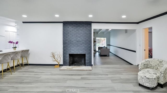 living area with crown molding, a brick fireplace, wood finished floors, and baseboards