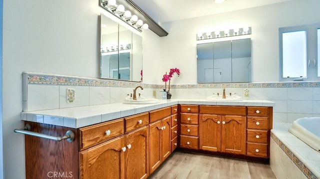 bathroom with a sink, wood finished floors, double vanity, and tiled bath