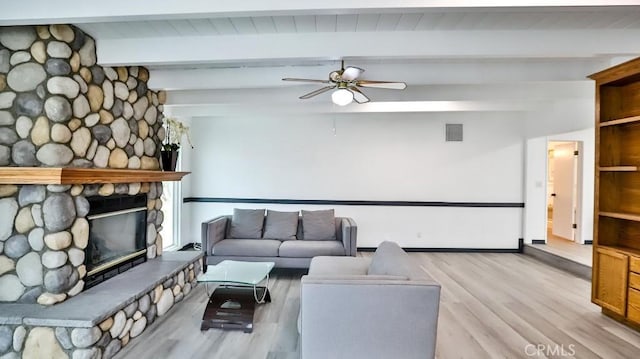 living room featuring light wood-type flooring, beam ceiling, a stone fireplace, and a ceiling fan