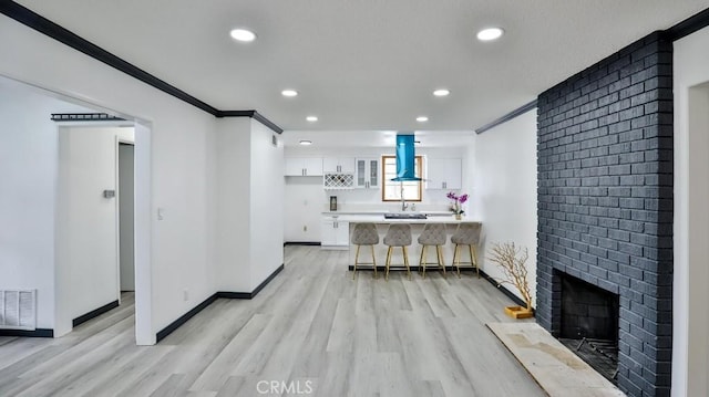 living area featuring light wood-type flooring, visible vents, crown molding, baseboards, and a brick fireplace