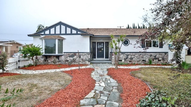 view of front of property with stone siding, stucco siding, a shingled roof, and fence