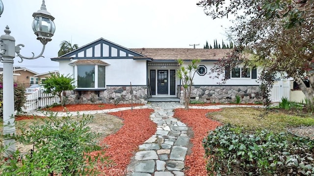 view of front of property with a shingled roof, fence, stone siding, and stucco siding