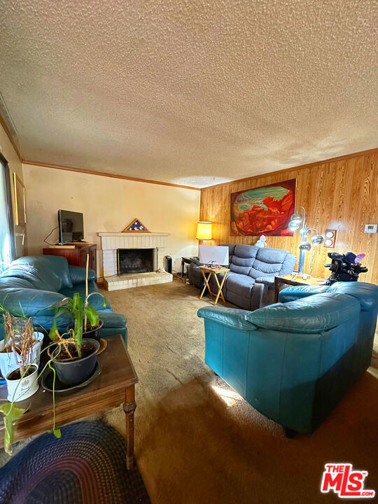 carpeted living room featuring a fireplace, a textured ceiling, crown molding, and wooden walls