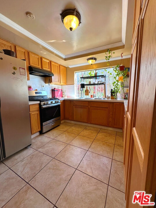 kitchen featuring stainless steel appliances, a raised ceiling, ornamental molding, and light tile patterned floors