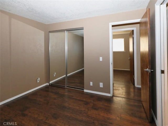 unfurnished bedroom with a textured ceiling, dark wood-type flooring, and a closet