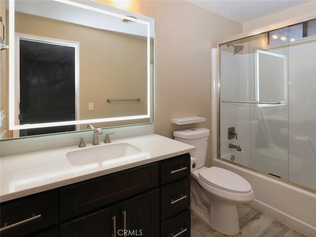 full bathroom featuring combined bath / shower with glass door, vanity, toilet, and hardwood / wood-style floors