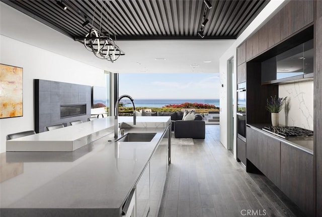 kitchen featuring sink, backsplash, a water view, stainless steel gas cooktop, and a center island with sink