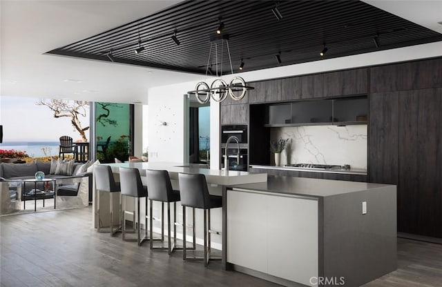 kitchen featuring dark hardwood / wood-style flooring, a notable chandelier, dark brown cabinets, and a center island with sink