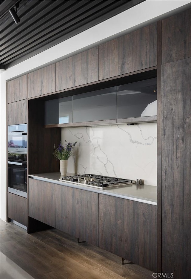 kitchen with dark wood-type flooring, double wall oven, stainless steel gas cooktop, and decorative backsplash