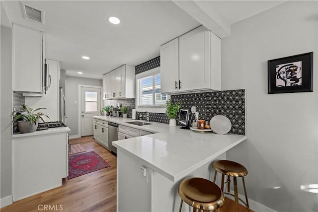 kitchen featuring white cabinets, sink, kitchen peninsula, stainless steel dishwasher, and a breakfast bar area