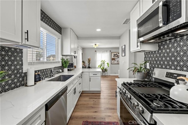 kitchen featuring kitchen peninsula, appliances with stainless steel finishes, wood-type flooring, white cabinets, and sink