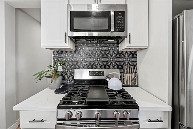 kitchen with stainless steel appliances, backsplash, white cabinetry, and light stone counters