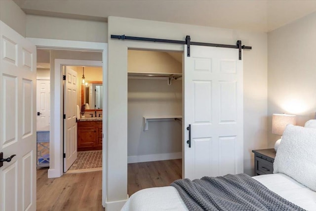 bedroom with ensuite bathroom, light hardwood / wood-style flooring, and a barn door