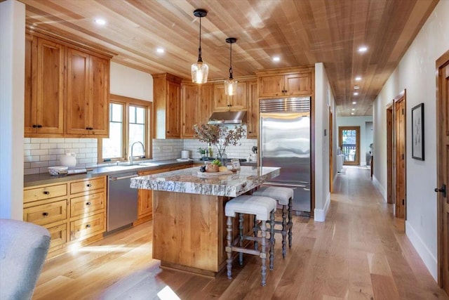 kitchen with a kitchen island, sink, hanging light fixtures, stainless steel appliances, and light stone counters