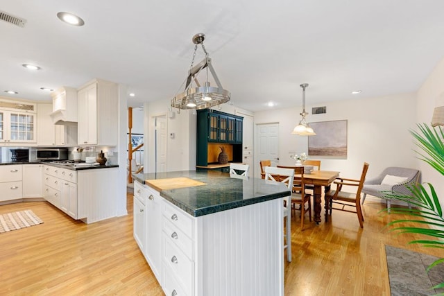 kitchen with white cabinets, decorative light fixtures, a kitchen bar, backsplash, and light wood-type flooring