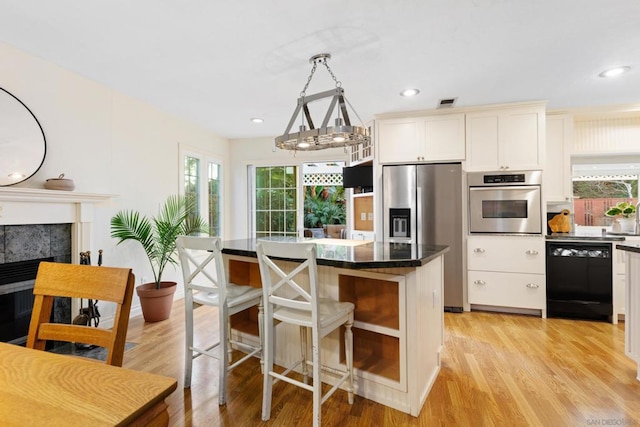 kitchen featuring light hardwood / wood-style floors, appliances with stainless steel finishes, a tiled fireplace, hanging light fixtures, and a center island