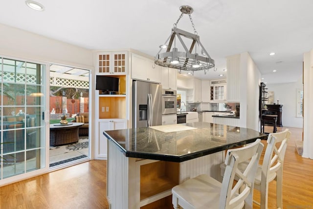 kitchen featuring decorative light fixtures, white cabinetry, stainless steel fridge, light wood-type flooring, and a breakfast bar