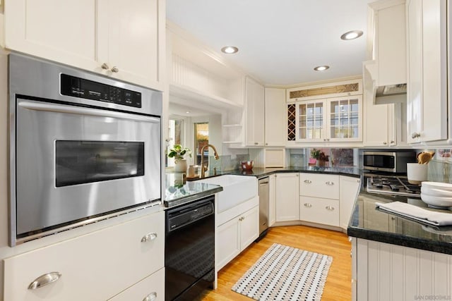 kitchen with white cabinets, stainless steel appliances, dark stone counters, light hardwood / wood-style floors, and sink