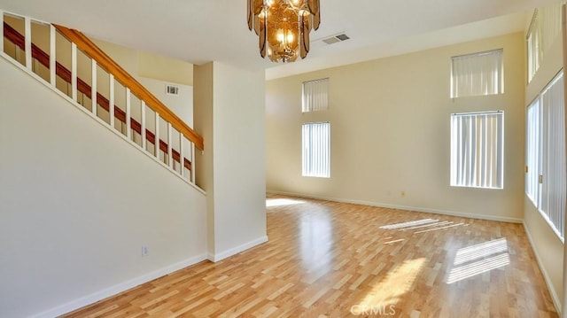 spare room with light wood-type flooring, an inviting chandelier, and a high ceiling