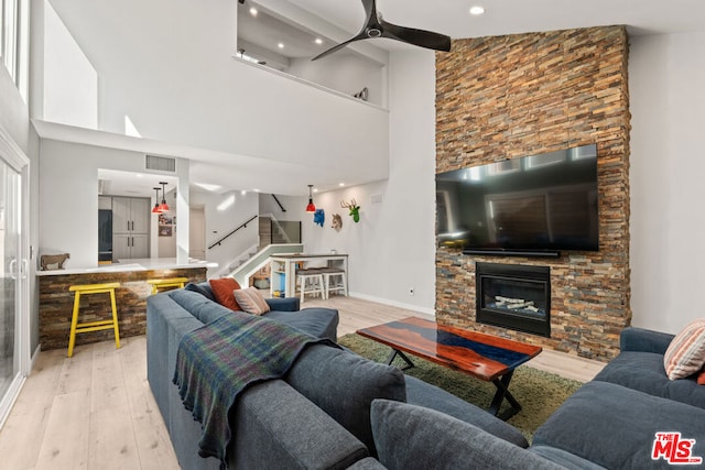 living room featuring light wood-type flooring, ceiling fan, a fireplace, and a high ceiling