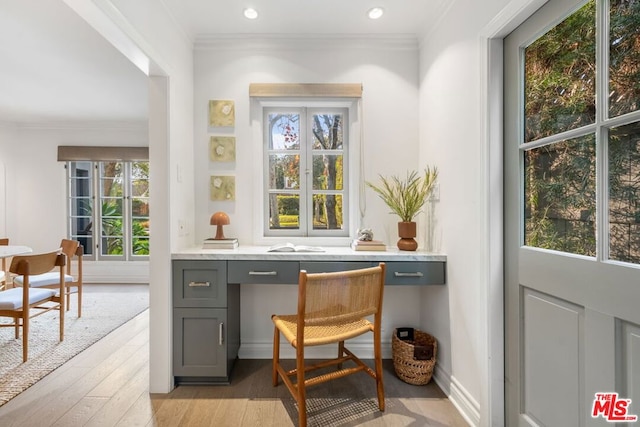 office with light wood-type flooring, ornamental molding, and built in desk