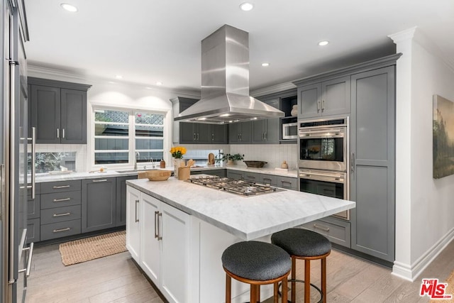 kitchen with appliances with stainless steel finishes, gray cabinets, island range hood, and a kitchen island